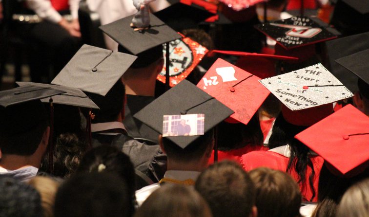 Photo of the tops of several graduates' mortarboards with decorations and a photo of a loved one