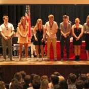 Top 10 students wearing their medallions and standing on stage in the high school auditorium, smiling