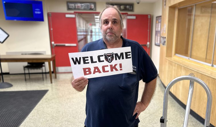 a custodial staff member smiling and holding a GF Nation Black Bears sign