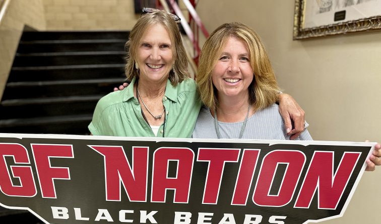 two school staff members smiling and holding a GF Nation Black Bears sign