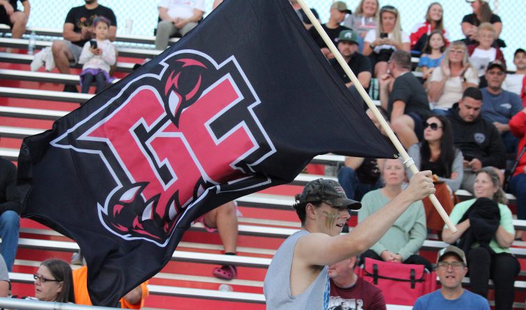 A student runs across the front row of the bleachers with the GF Black Bears flag