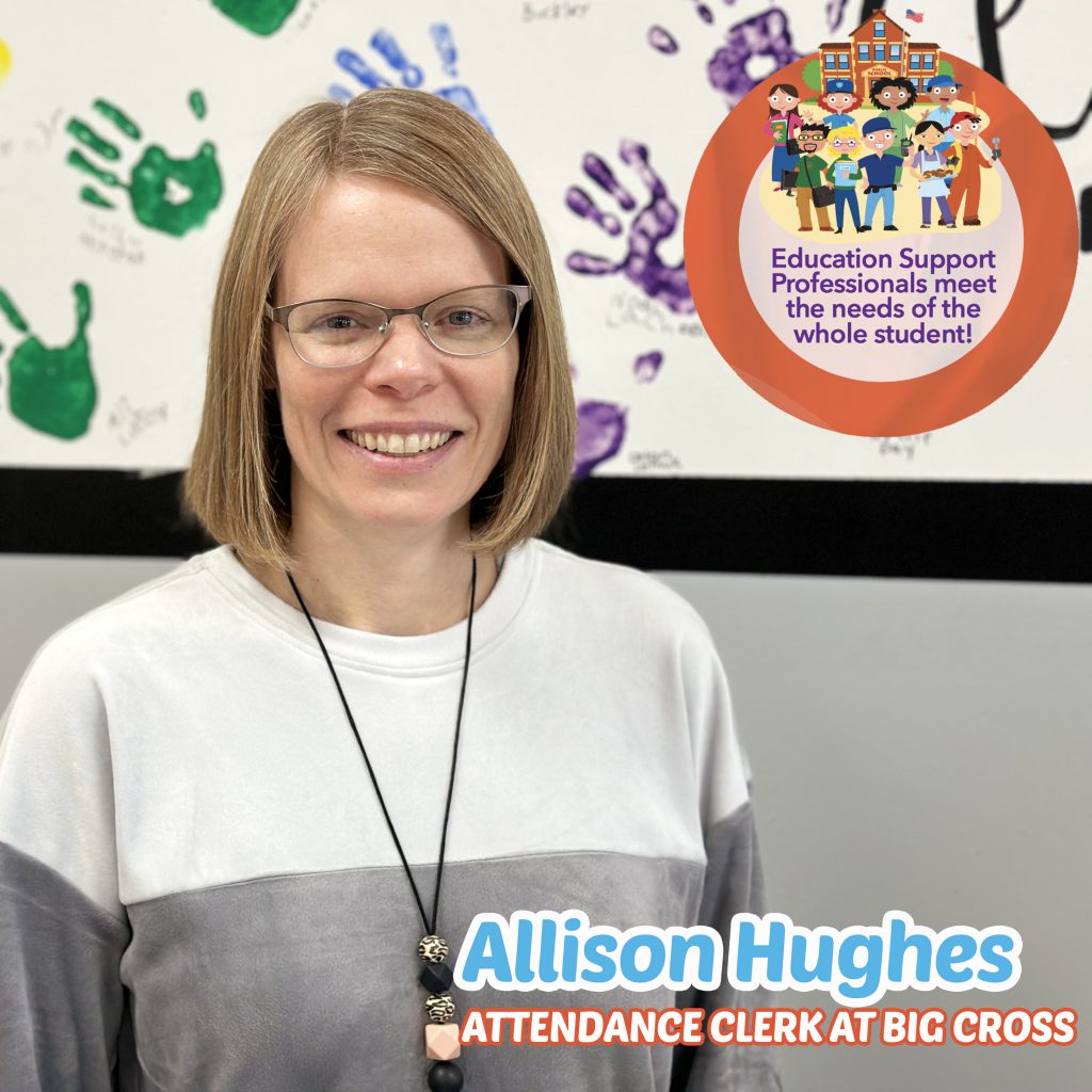 Mrs. Huighes smiling in the cafeteria in front of brightly colored handprints on the wall