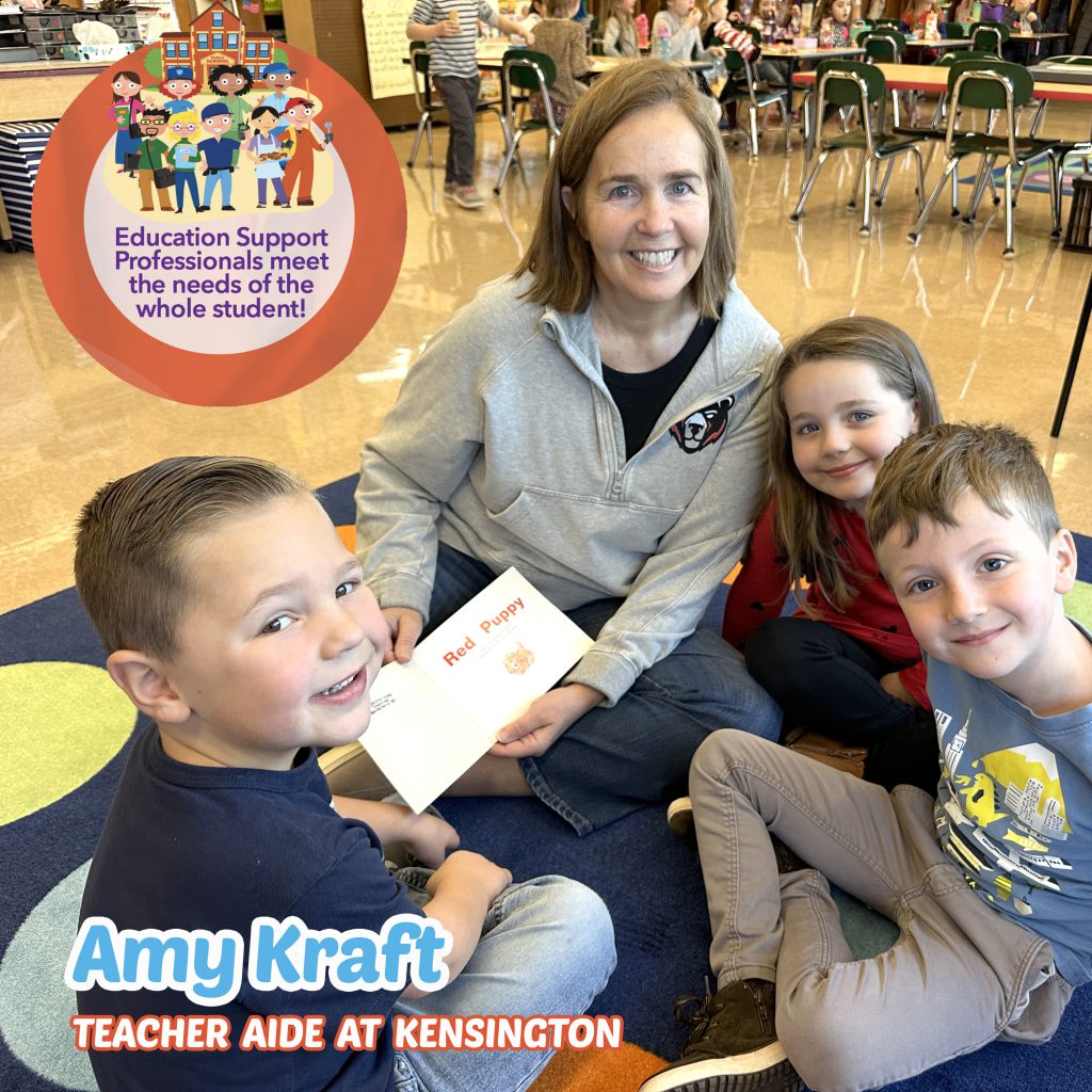 Mrs. Kraft sitting on the classroom rug with students smiling as they read a book together