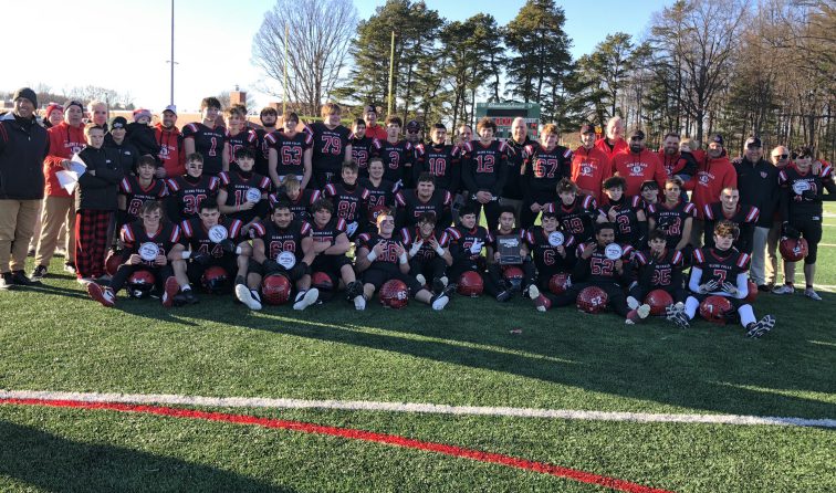 FOotball team holding up white section championship patches and smiling